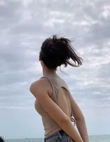 她坐在沙滩上，双手后撑，仰头感受微风，动作随意自然，尽显惬意假日氛围
